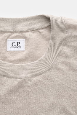 C.P. Company Kurzarmpullover grau, Nahaufnahme des Rundhalsausschnitts mit feinem Leinenstrick, elastischen Rippbündchen und kleinem Weblabel am Saum, Regular Fit, weicher Griff, feines Strickbild, fotografiert von oben.