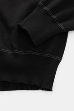 Nahaufnahme aus schräger Perspektive des Ärmels und Bunds vom schwarzen C.P. Company Rundhalspullover mit kontrastierenden weißen Nähten.
