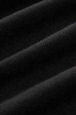 Nahaufnahme der schwarzen, fein gestrickten Baumwollstruktur des C.P. Company Rundhalspullover schwarz, im Detail und schräger Perspektive.