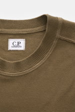 Nahaufnahme des olivfarbenen C.P. Company Rundhalspullover, fotografiert aus schräger Draufsicht, mit feinem Strick und Label innen.