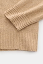 Close-up image of the sleeve and lower hem of the 04651/ A trip in a bag Rundhalspullover 'Knit Terry Crew' beige, showing its fine bouclé structure and ribbed cuffs, photographed from above. Markante Frottee-Optik: Der feine Bouclé-Strick aus elastischer