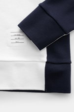 Nahaufnahme von Ärmeln und Label des Thom Browne Rundhals-Sweatshirts weiß/navy, fotografiert von oben, mit weichem Baumwollstoff, Regular Fit, Rundhalsausschnitt, kontrastierenden Ärmeln, rückwärtiger Grosgrain-Schlaufe und komfortablen Rippbündchen.
