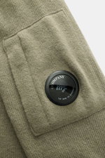 Nahaufnahme des C.P. Company Rundhalspullover graugrün Ärmels mit mittelfeinem Strickbild, Tasche mit Zipper und labeltypischem Linsen-Detail.