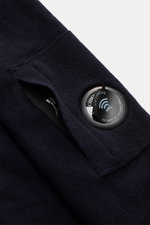 C.P. Company Rundhalspullover navy, Nahaufnahme von Ärmeltasche mit Reißverschluss und schwarzem NFC-Linsen-Detail, feiner Woll-Mix.