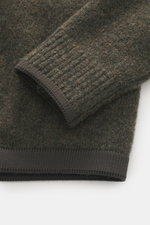 Nahaufnahme des Ärmels vom Stone Island Rundhalspullover 'Stellina' dark olive, fotografiert von oben, Mix aus Schurwolle und Microfaser, weicher Griff, Regular Fit, Rundhalsausschnitt, Raglanärmel, dezentes Stellina-Stitching.