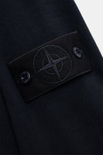 Nahaufnahme des tonalen Kompass-Badges am Oberarm des Stone Island Rundhalspullover 'Ghost Piece' navy aus reiner Wolle, Slim Fit, mit feinem Strickbild und elastischen Rippbündchen, fotografiert von schräg oben.