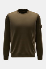 Stone Island Rundhalspullover 'Ghost Piece' dark olive, Slim Fit aus weicher Wolle, fein gestrickt, frontale Nahaufnahme mit Kompass-Badge am Oberarm.