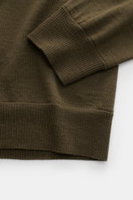 Nahaufnahme des Stone Island Rundhalspullover 'Ghost Piece' dark olive in Slim Fit, fotografiert von oben auf Ärmel und Saum aus reiner Wolle.