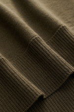 Nahaufnahme des Stone Island Rundhalspullover 'Ghost Piece' dark olive von oben, feines Strickbild, reine Wolle, weicher Griff, Slim Fit, elastische Rippbündchen sichtbar.