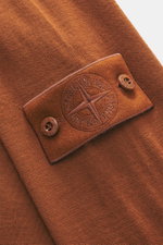 Nahaufnahme des Stone Island Rundhalspullover 'Ghost Piece' rostbraun aus reiner Wolle mit feinem Strickbild, tonalem Kompass-Badge und Knöpfen, fotografiert von schräg oben.