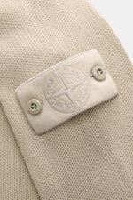 Stone Island Rundhalspullover 'Ghost Piece' sand, Detailaufnahme von tonalem Kompass-Badge mit Knöpfen, mittelfeines Strickbild aus Baumwoll-Cashmere-Mix, weicher Griff.