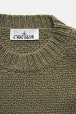 Nahaufnahme von Stone Island Rundhalspullover oliv aus RWS-zertifizierter Schurwolle und Microfaser mit voluminösem Strickbild, Rundhalsausschnitt, elastischen Rippstrickbündchen und Kompass-Badge, fotografiert von oben.