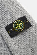 Nahaufnahme des Stone Island Rundhalspullover grau von schräg oben, Strick aus RWS-zertifizierter Schurwolle und Microfaser, leicht strukturierter Griff, voluminöses Strickbild, Regular Fit, Rundhalsausschnitt, Kompass-Badge am Oberarm, elastische Rippstr