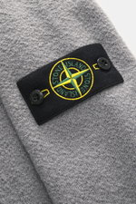 Nahaufnahme des Stone Island Rundhalspullover 'Maglia' grau, weiche reine Wolle, mittelfeines Strickbild, Kompass-Badge am Oberarm, von oben fotografiert.