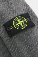 Nahaufnahme des Stone Island Rundhalspullover 'Chenille' dunkelgrau, Detail des Kompass-Badges am Oberarm, grobes Baumwoll-Chenille-Strick.