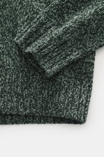 Nahaufnahme des Stone Island Rundhalspullover 'Chenille' dunkelgrün/salbei meliert, seitlich fotografiert, mit weichem Chenille-Strick, rolliertem Ausschnitt und Kompass-Badge am Ärmel.