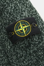 Nahaufnahme des Stone Island Rundhalspullover 'Chenille' dunkelgrün/salbei meliert mit grobem Chenille-Strick, weichem Griff und Kompass-Badge am Ärmel.