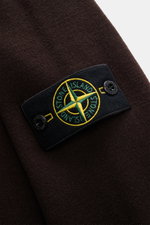 Close-up detail of the Stone Island Dark Brown Crew Neck Sweater showing the signature compass badge on the upper arm, photographed from a side angle.

Description:
<p>Warming comfort with iconic character: This STONE ISLAND sweater combines a premium woo
