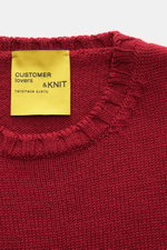 Close-up top-down view of the B.F. Knitwear Merino crew neck jumper red showing rib knit bands and yellow label, pure merino wool, soft feel, semi chunky knit, slim fit, crew neck.