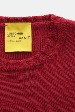 Close-up top-down view of the B.F. Knitwear Merino crew neck jumper red showing rib knit bands and yellow label, pure merino wool, soft feel, semi chunky knit, slim fit, crew neck.