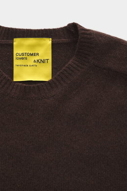 Close-up photo from above of the B.F. Knitwear Cashmere crew neck sweater dark brown showing the ribbed crew neckline and yellow label.