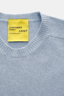 Close-up front view of B.F. Knitwear Cashmere crew neck sweater light blue melange showing crew neckline and knit texture, pure cashmere, soft touch, medium-fine knit, slim fit, elastic ribbed cuffs, durable, made in Italy.