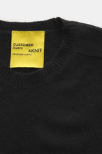 Close-up top-down view of B.F. Knitwear Cashmere crew neck sweater black, showing soft medium-fine knit, ribbed cuffs, and yellow label.

Description: <p>Autumnal cashmere from the knitting expert B.F. KNITWEAR: This softly knitted crew neck sweater is th
