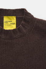 Close-up front view of B.F. Knitwear Cashmere crew neck sweater dark brown showing medium coarse knit and ribbed neckline with yellow label.