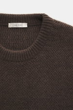 Close-up front view of The Row Crewneck sweater 'Anish' gray-brown melange showing textured pearl knit, crew neckline, and soft ribbed cuffs.