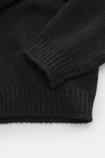 Close-up front-side view of The Row Cashmere crewneck sweater 'Markhim' dark gray melange showing its coarse knit pattern, ribbed cuffs, and dense texture, made of slightly elastic, soft-touch cashmere with an oversized fit and crew neckline. Statement kn