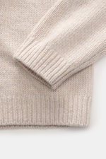 Nahaufnahme des Maison Kitsuné Rundhalspullovers sand meliert, Detailansicht von Ärmel und Saum aus weichem, mittelfeinem Wollstrick mit Rippbündchen, fotografiert von oben.