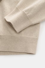 Close-up top-down view of Jacquemus Merino crew neck sweater beige melange sleeve and hem, showing elastic merino wool, soft touch, medium-fine knit pattern, regular fit, crew neckline, logo detail on the back, and comfortable ribbed cuffs.
