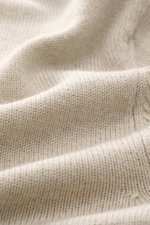 Close-up fabric texture of Jacquemus Merino crew neck sweater beige melange, photographed from above, showing elastic merino wool, soft touch, medium-fine knit pattern, regular fit, crew neckline, logo detail on the back, and comfortable ribbed cuffs.