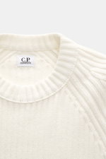 C.P. Company Rundhalspullover creme, Nahaufnahme von oben, Rippstrick aus reiner Baumwolle, weiche Qualität, mittelfeines Strickbild, Slim Fit, Raglanärmel, Tasche am Ärmel, labeltypisches Linsen-Detail.