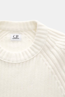 C.P. Company Rundhalspullover creme, Nahaufnahme von oben, Rippstrick aus reiner Baumwolle, weiche Qualität, mittelfeines Strickbild, Slim Fit, Raglanärmel, Tasche am Ärmel, labeltypisches Linsen-Detail.