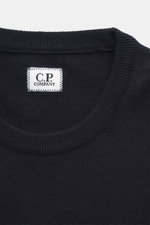 Nahaufnahme des C.P. Company Rundhalspullover navy von oben, Slim Fit, weicher Griff, feines Strickbild, Rundhalsausschnitt, flexible Rippbündchen, Mix Schurwolle, Tasche mit Druckknopf, Linsen-Detail.