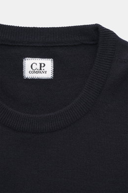Nahaufnahme des C.P. Company Rundhalspullover navy von oben, Slim Fit, weicher Griff, feines Strickbild, Rundhalsausschnitt, flexible Rippbündchen, Mix Schurwolle, Tasche mit Druckknopf, Linsen-Detail.