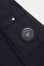 Nahaufnahme des navy C.P. Company Rundhalspullover Slim Fit aus Schurwolle und Microfaser, weicher Griff, feines Strickbild, Rundhalsausschnitt, Tasche mit Druckknopf am Oberarm, labeltypisches Linsen-Detail und flexible Rippbündchen, seitliche Perspektiv