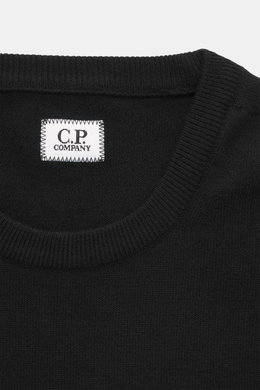 Nahaufnahme des C.P. Company Rundhalspullover schwarz, Frontansicht mit Rundhalsausschnitt, feinem Strickbild, weichem Griff, Slim Fit, Tasche am Oberarm, flexible Rippbündchen, Mix aus Schurwolle und Microfaser, labeltypisches Linsen-Detail.