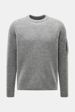 C.P. Company Rundhalspullover grau meliert, frontal fotografiert, mittelfeines Strickbild, Mix aus Wolle und Microfaser, Slim Fit, weicher Griff, elastisch, Zipper-Tasche am Oberarm, flexible Rippbündchen, labeltypisches Linsen-Detail.