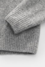 Nahaufnahme des C.P. Company Rundhalspullover grau meliert von oben, zeigt weichen, voluminösen Griff mit mittelfeinem Strickbild, flexible Rippbündchen, Mix aus Wolle und hochwertiger Microfaser, elastische Qualität, Slim Fit, Zipper-Tasche am Oberarm un