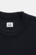 C.P. Company Rundhalspullover navy, Nahaufnahme von oben, mittelfeines Strickbild, markantes Patent-Strickmuster, weicher Griff, Rundhalsausschnitt, labeltypisches Linsen-Detail.