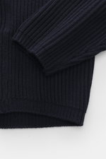 Nahaufnahme des C.P. Company Rundhalspullover navy, fotografiert von schräg oben, zeigt Strick aus Schurwolle und Microfaser, weicher Griff, mittelfeines Strickbild, patent-Strickmuster, Slim Fit, Rundhalsausschnitt, Tasche mit Zipper am Oberarm, labeltyp