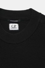 C.P. Company Rundhalspullover 'Metropolis' schwarz, Nahaufnahme von oben zeigt Waffelstrick aus Schurwolle und Microfaser, feines Strickbild, kerniger Griff, Regular Fit, Rundhalsausschnitt, Ärmeltasche mit Logo-Patch, flexible Rippbündchen.