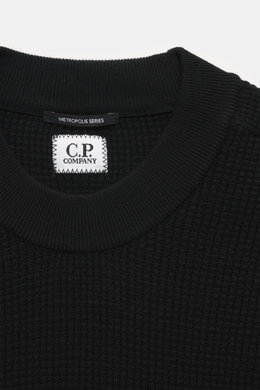 C.P. Company Rundhalspullover 'Metropolis' schwarz, Nahaufnahme von oben zeigt Waffelstrick aus Schurwolle und Microfaser, feines Strickbild, kerniger Griff, Regular Fit, Rundhalsausschnitt, Ärmeltasche mit Logo-Patch, flexible Rippbündchen.