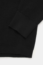 Nahaufnahme des C.P. Company Rundhalspullover 'Metropolis' schwarz Ärmels, Waffelstrick aus Schurwolle und Microfaser, feines Strickbild, kerniger Griff, Regular Fit, Rundhalsausschnitt, Ärmeltasche mit Logo-Patch, flexible Rippbündchen.