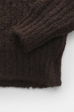 Nahaufnahme des Kiefermann Rundhalspullover 'Yakub' dunkelbraun mit grobem Strickbild, weichem Griff, Rippbündchen, Oversized Fit, aus Microfaser, Alpaka und Wolle, fotografiert von oben.