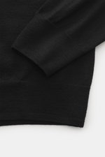 Close-up image from a top-down perspective of the B.F. Knitwear Merino Crew Neck Sweater black showing the sleeve and ribbed cuff, highlighting pure merino wool, soft feel, fine knit pattern, regular fit, crew neckline, and comfortable ribbed cuffs.