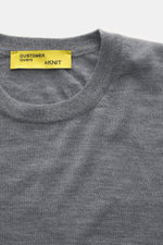 Close-up top-down view of B.F. Knitwear Merino Crew Neck Sweater grey melange showing crew neckline, pure merino wool, soft feel, fine knit pattern, regular fit, comfortable ribbed cuffs, and yellow label.