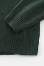 Nahaufnahme des dunkelgrünen 04651/ A trip in a bag Rundhalspullovers mit Merinowolle-Cashmere-Mix, feinem Strick, Rippbündchen und eingestrickter Tasche, fotografiert von oben.